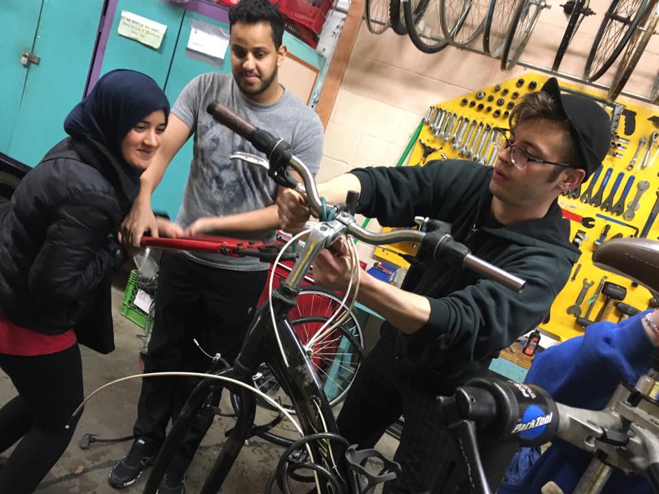 Three people working together on a bicycle in the Bike Project workshop